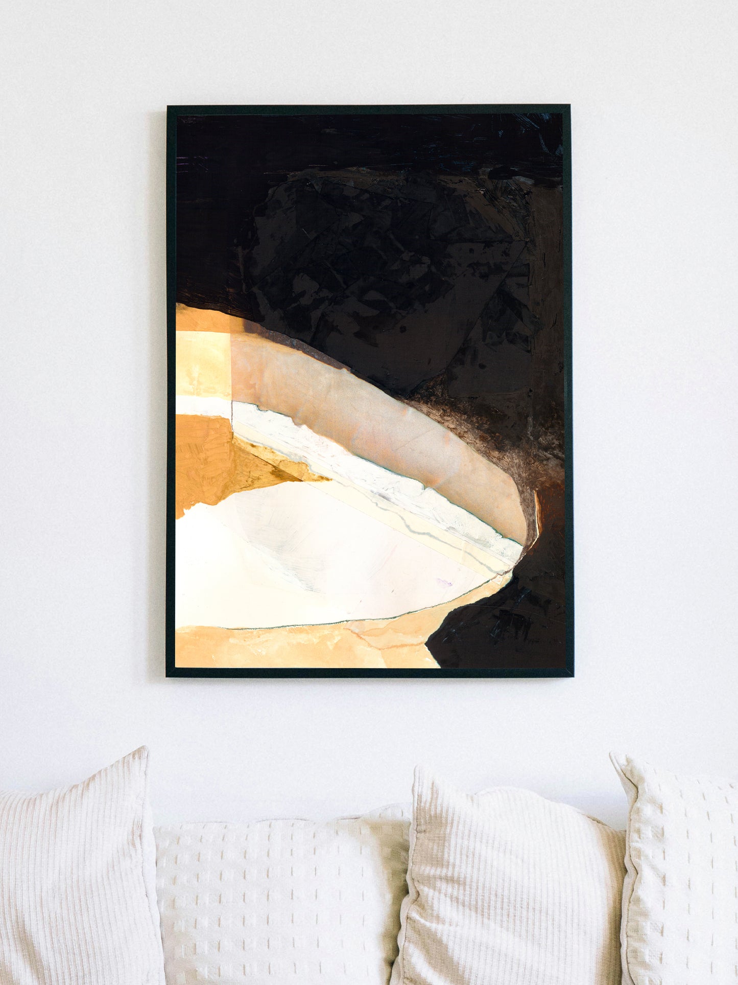 Abstract art print with black, gold, and white colors on a white wall above a sofa.