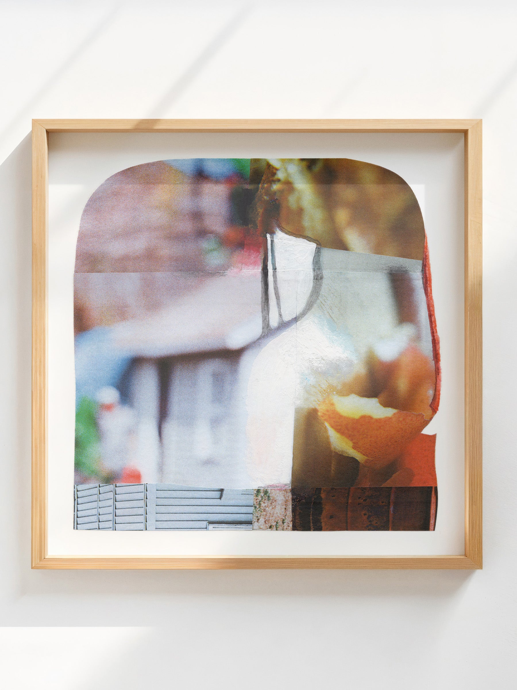 Square mixed media abstract collage with bright colors in an oak frame on a white wall.