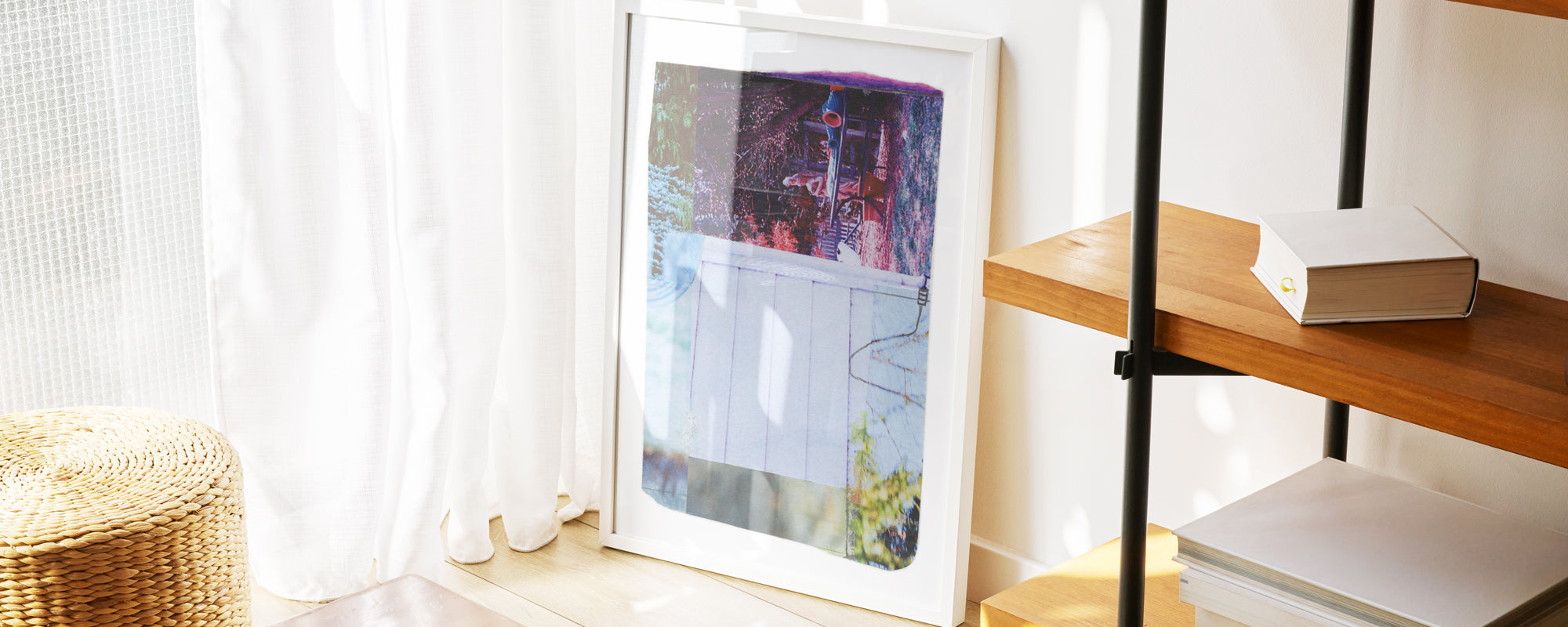 Framed colorful collage leaning on a wall next to a white curtain.