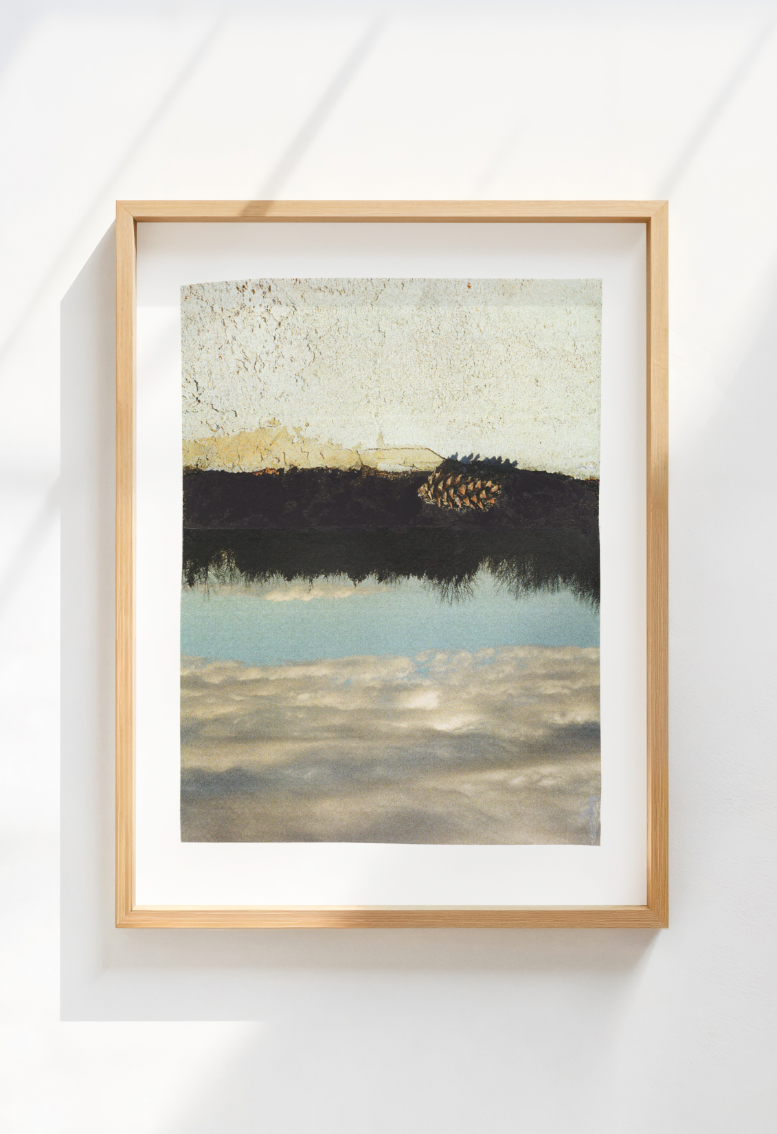 Framed abstract collage with a landscape of stucco, trees, and sky with a pine cone.