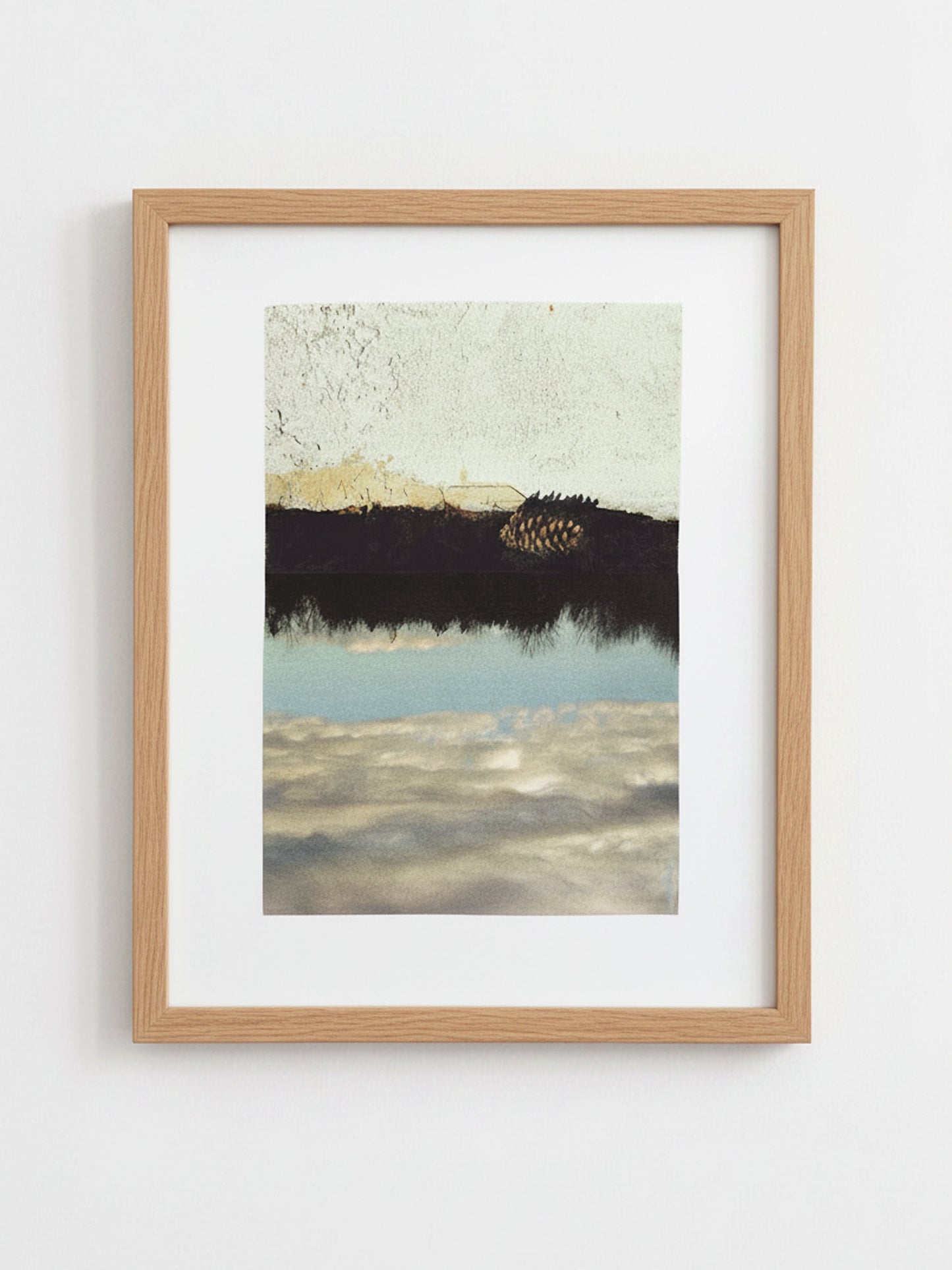 A framed art print featuring an abstract landscape with a dark horizontal band, a pale sky, and reflective water, presented in a light natural wood frame with a white mat against a white wall.