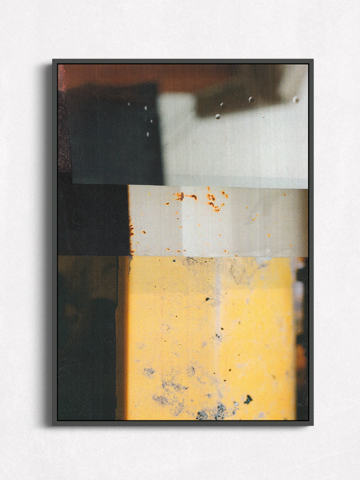 A framed abstract geometric wall art print featuring blocks of yellow, black, white, and brown with distressed textures, displayed on a light gray wall.