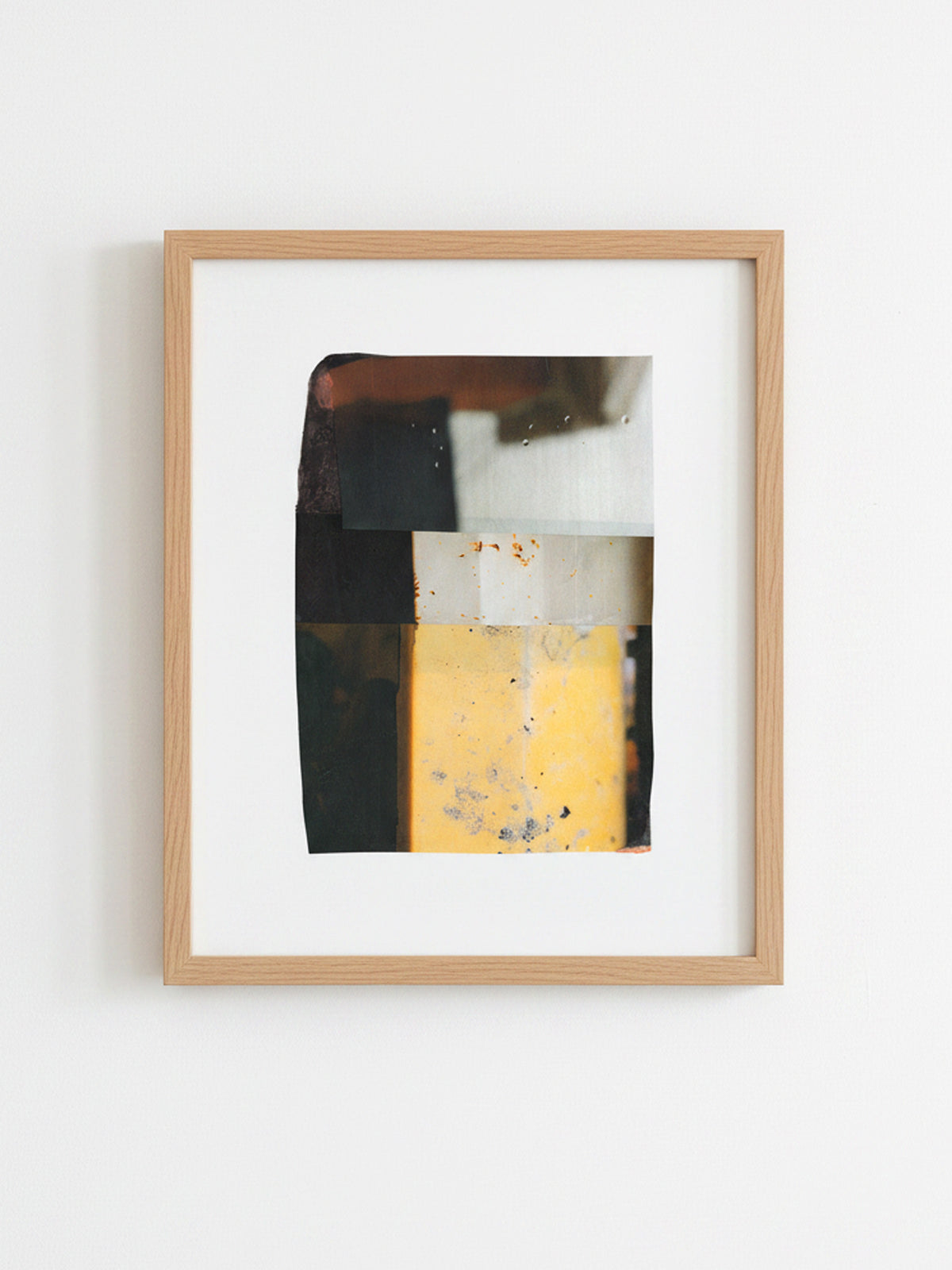 A framed abstract art print featuring a geometric color-blocked design in black, white, yellow, and brown, set in a light natural wood frame against a white wall.