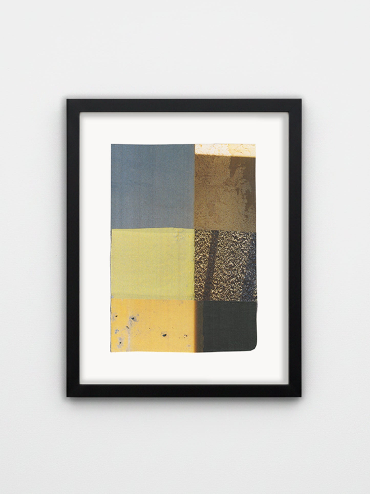A framed abstract art print featuring a grid of textured blocks in muted blue, yellow, brown, and black, presented in a black frame with a white mat against a light gray wall.
