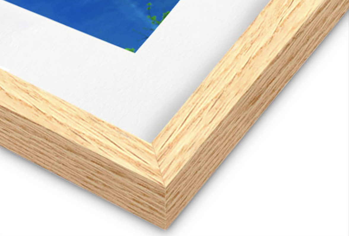 Close-up of a oak picture frame corner with a white border around the artwork.