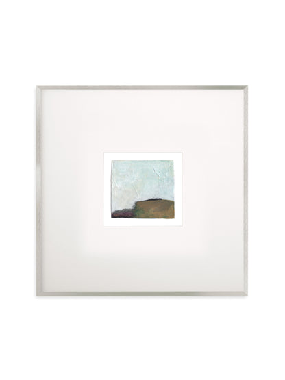 A square framed abstract art print featuring a textured light blue and brown landscape, presented with a wide white mat and a thin silver frame against a white background.