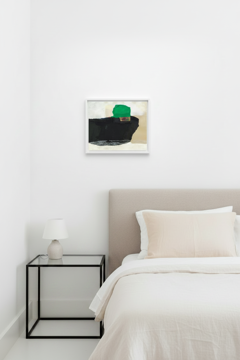 A framed abstract art print featuring a black block, beige background, and a green geometric shape, displayed on a white wall above a bed with a beige headboard and white bedding in a modern bedroom setting.