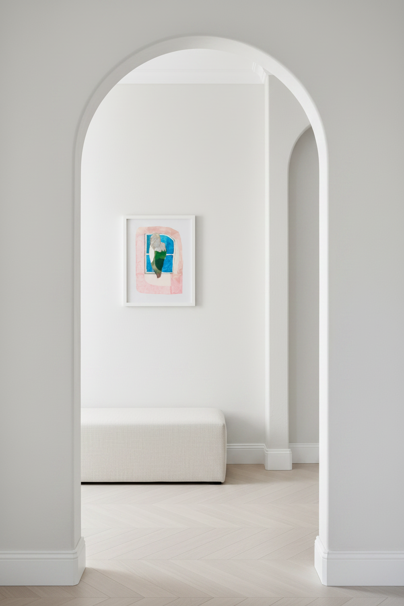 A minimalist interior scene viewed through a white arched doorway, showing a small white bench against a white wall with a framed abstract artwork in pink, blue, and green tones. Light wood herringbone flooring and clean white trim complete the space.
